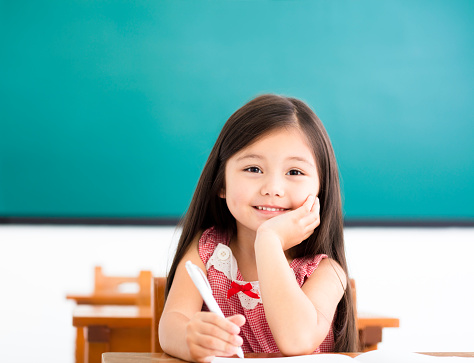 happy little girl writing at desk in classroom