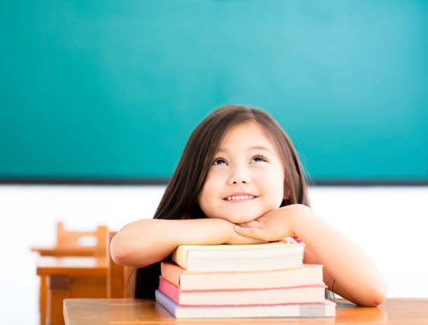 petite fille heureuse avec des livres et la pensée dans la salle de classe - blackboard child thinking little girls photos et images de collection