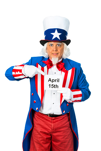 A patriotic Uncle Sam character pointing to a sign he is holding that reads April 15th, which is tax day in the US. He is wearing a red, white and blue coat and top hat that has a blue ban and white star while standing in from of a white background.