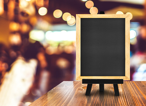 Blackboard with easel on wood table at blurred coffee shop background,Mock up for display or montage of design for online shopping promotion.