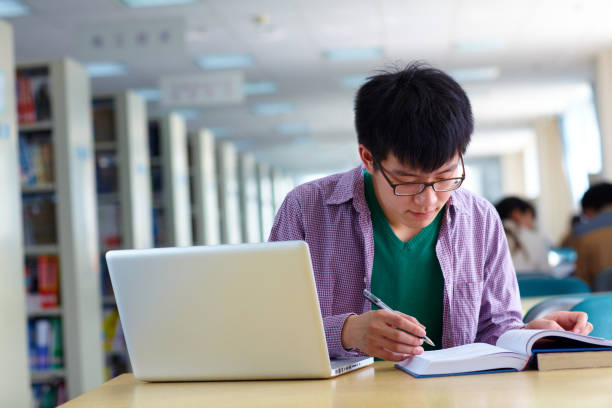 istock One male asian college student study in the library with laptop on table 666823792