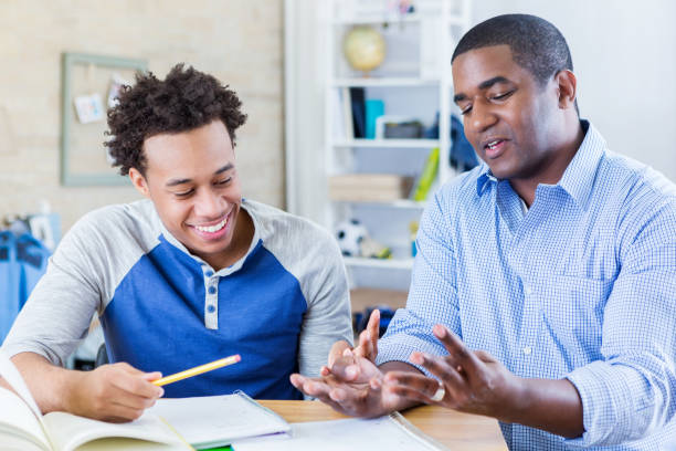 Dad helps teenage son with homework Mid adult African American dad helps teenage sone with homework assignment. The dad gestures while explaining something to his son. college student and parent stock pictures, royalty-free photos & images