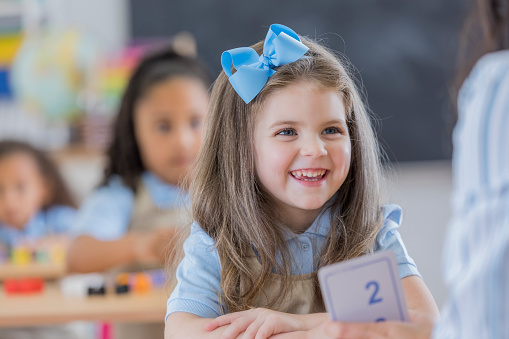 Cheerful Caucasian young schoolgirl smiles while using flashcards at school.