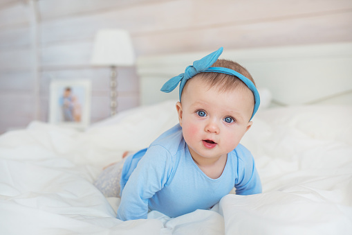 Smiling infant in blue clothes crawls on a bed in bedroom
