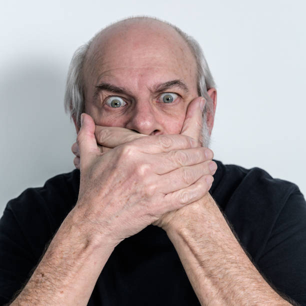 Speak No Evil Senior Adult Man Hands Covering Mouth A stubborn, staring, silent senior adult man is covering his mouth with his hands - quite firmly. Mr. Speak No Evil clearly has no intention of talking or saying anything at all. speak no evil stock pictures, royalty-free photos & images