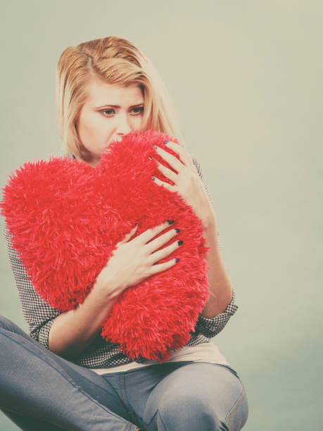 istock Sad woman holding red pillow in heart shape 666878560