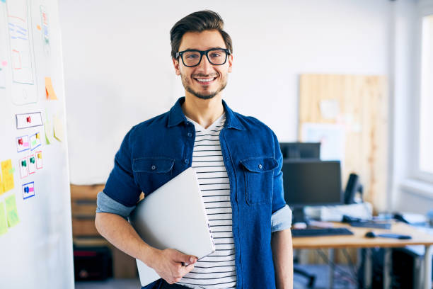 szczęśliwy młody człowiek, projektant stron internetowych stojący z laptopem - men holding smiling young adult zdjęcia i obrazy z banku zdjęć