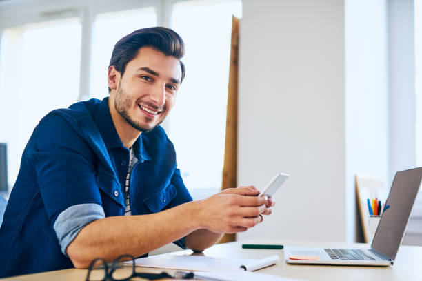 homens, verificando seu smartphone no escritório, sentado na mesa com o computador portátil - computer programmer laptop men nerd - fotografias e filmes do acervo