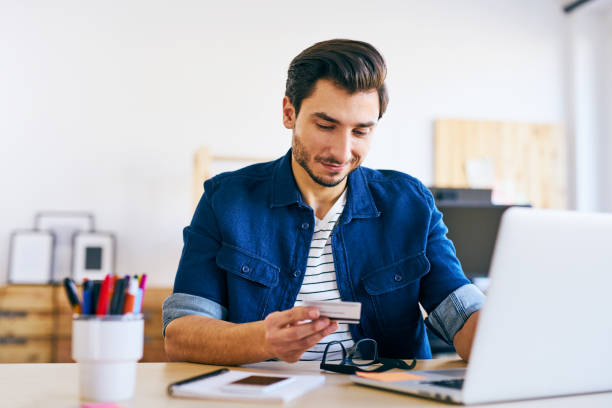 istock Young man doing online payments typing number from his credit card 666890182