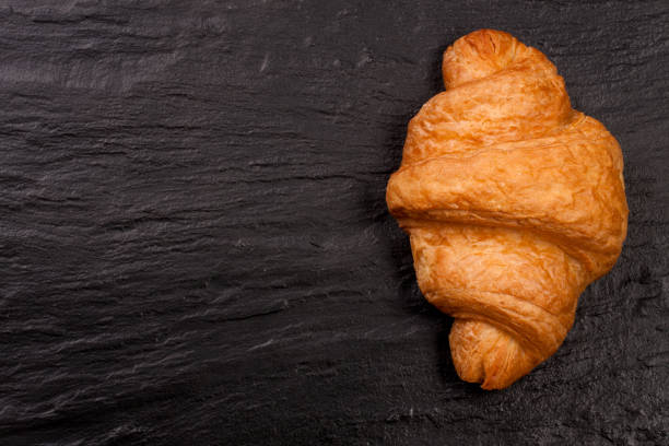istock one croissant on black stone background with copy space for your text. Top view 666890234
