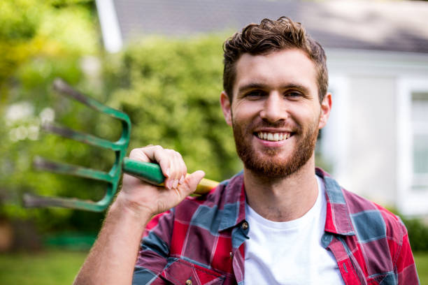 Close-up portrait of smiling man with rake standing in yard