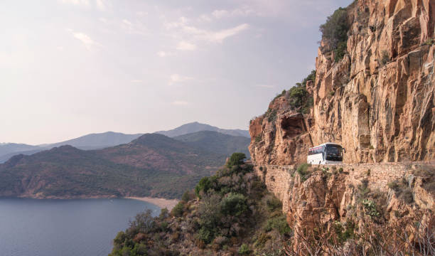 A white tourist bus on a Mediterranean mountain road on a cliff of a sunny bay