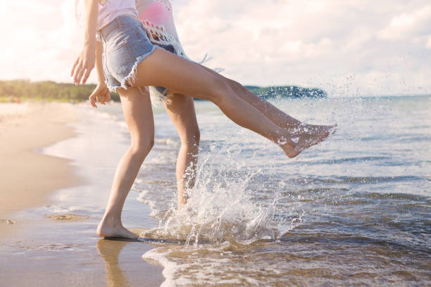 istock Two girls standing barefoot in the sea splashing 666908328