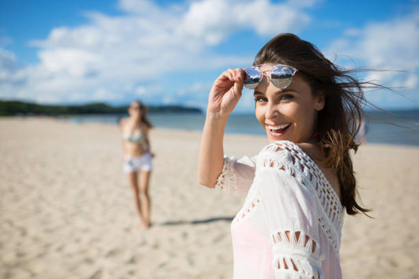 happy beautiful woman standing on beach with friend laughing - women smiling body cheerful imagens e fotografias de stock