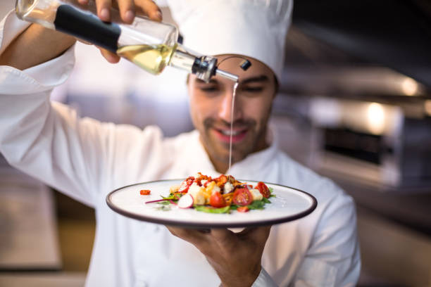 guapo chef verter aceite de oliva en la comida - chef fotografías e imágenes de stock