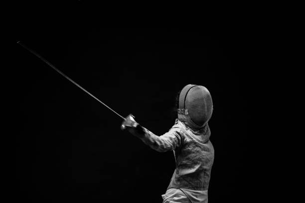 Sporting Women practicing Fencing sport  Women in sport Young woman Fencer action in fencing pose   Black background BW Sporting Women practicing Fencing sport  Women in sport Young woman Fencer action in fencing pose   Black background BW sword photos stock pictures, royalty-free photos & images