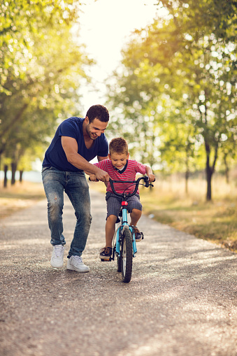 Small boy enjoying at the park with his father while learning to ride a bicycle.
