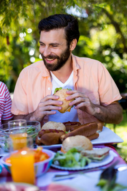 istock Happy man sitting with sandwich at table in yard 666919312