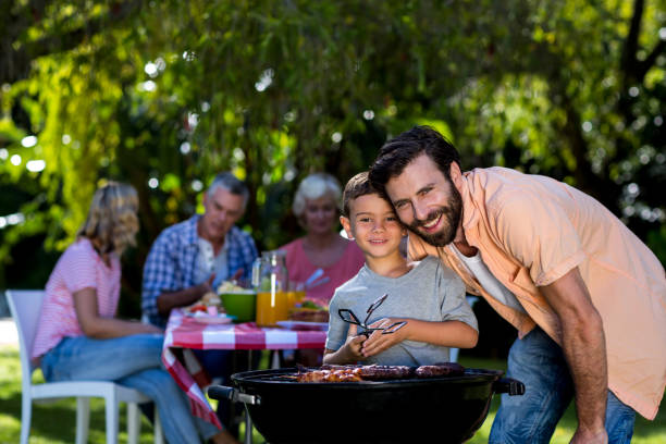 istock Smiling father with son by barbecue grill in yard 666923692