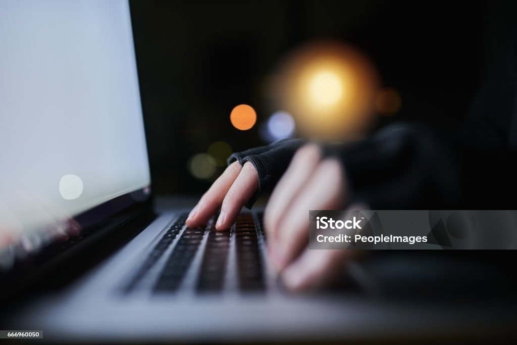 Be careful what you share online Shot of an unrecognizable computer hacker using a laptop late at night Dishonesty Stock Photo