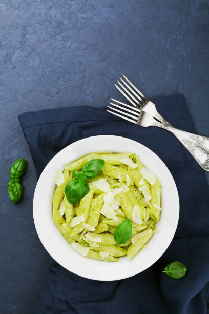 Pasta with pesto sauce decorated basil leaves and parmesan cheese. Food background with empty space for you recipe. Flat lay.