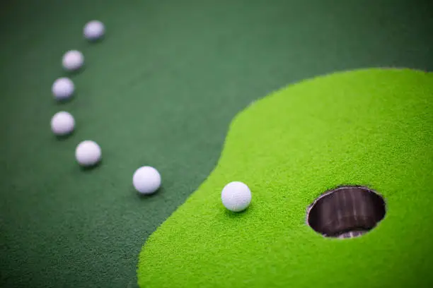 Photo of Golf Balls Curving Towards Hole. Goal. Win.