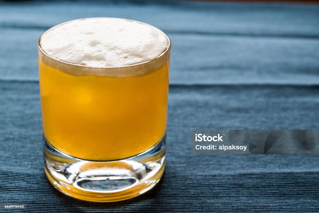 Cóctel de whisky Sour con fondo azul y espuma. - Foto de stock de Sabor amargo libre de derechos