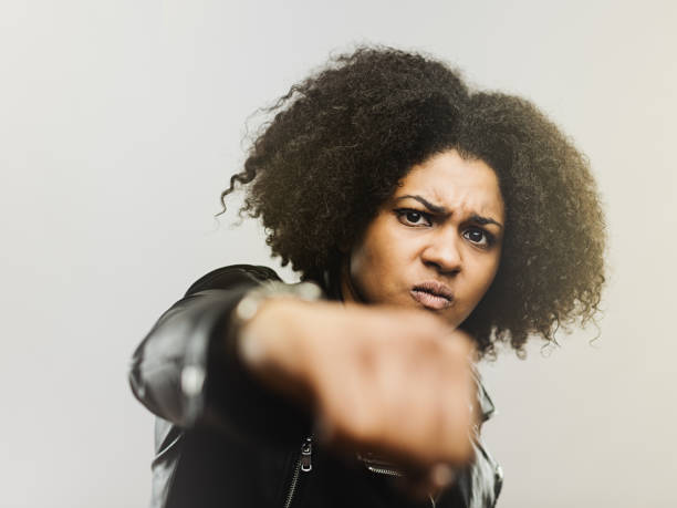 Horizontal portrait of angry black woman boxing at camera. Close up of aggressive real woman fighting against gray background. Studio photography from a DSLR camera. Sharp focus on eyes.