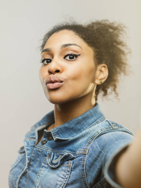 Vertical portrait of beautiful young african american woman taking a selfie. Real woman making selfie and pouting against gray background.  Studio photography from a DSLR camera. Sharp focus on eyes.