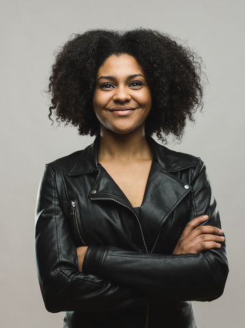 Portrait of beautiful afro american woman smiling with her arms crossed against gray background. Vertical shot of real woman posing confidently. Studio photography from a DSLR camera. Sharp focus on eyes.