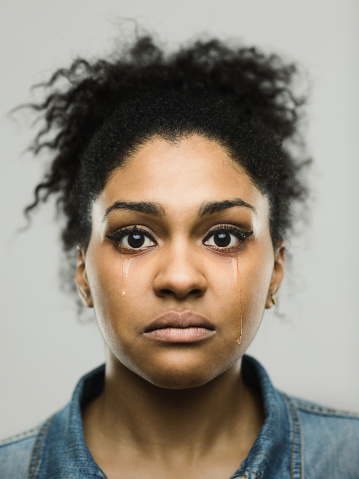 Close-up portrait of sad young afro american woman. Crying female against gray background with tears in her face. Vertical studio photography from a DSLR camera. Sharp focus on eyes.