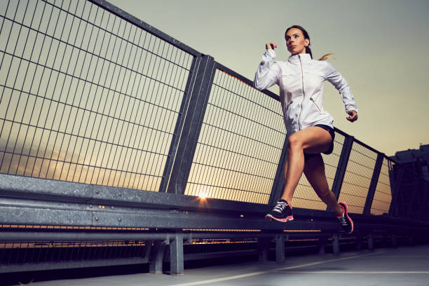 femme athlétique courant pendant le coucher du soleil sur le toit du stationnement, garage - jumping women running vitality photos et images de collection