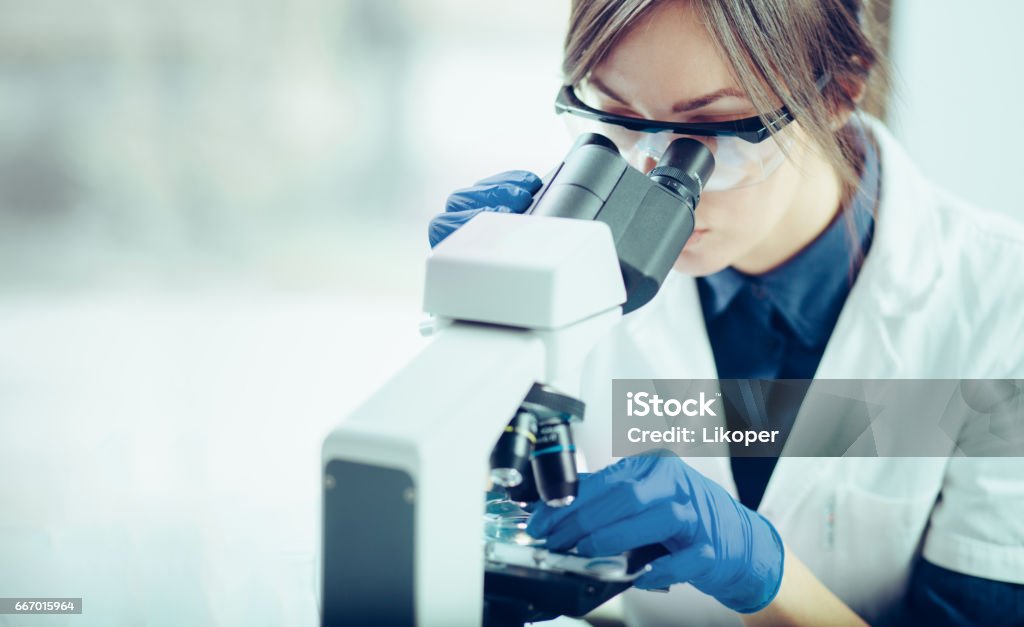 Young scientist looking through a microscope in a laboratory. Young scientist doing some research. Microscope Stock Photo