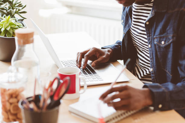 młody człowiek pracujący na laptopie i robienie notatek - typing using computer computer keyboard computer zdjęcia i obrazy z banku zdjęć