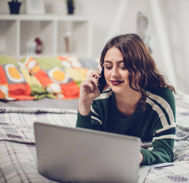 istock Woman talking on mobile phone and using laptop in bed 667021288