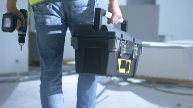 Construction Worker Walking inside Building Under Construction and Carrying Toolbox