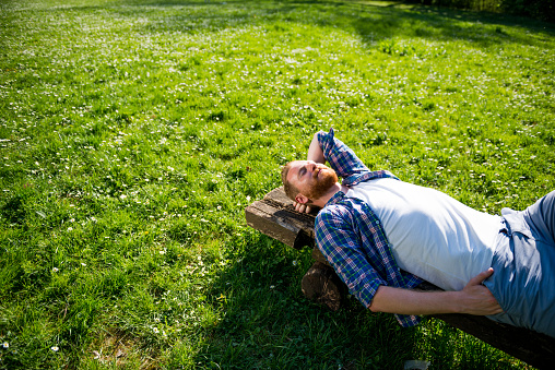 Man lying on green grass with his hands under his head, enjoying summer.