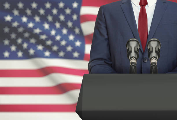 Businessman or politician making speech from behind a pulpit with national flag on background - United States stock photo