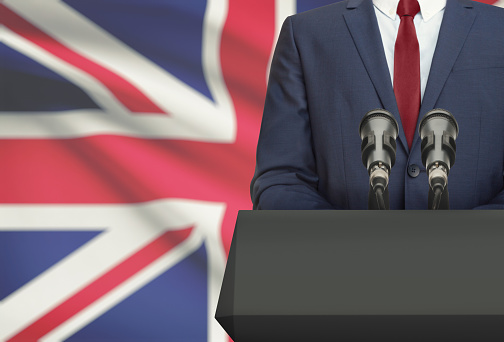 Businessman or politician making speech from behind the pulpit with national flag on background - United Kingdom