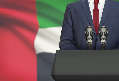 Businessman or politician making speech from behind the pulpit with national flag on background - United Arab Emirates