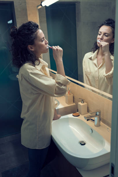istock Woman brushing teeth in bathroom mirror 667037816