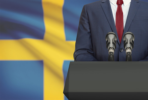 Businessman or politician making speech from behind the pulpit with national flag on background - Sweden