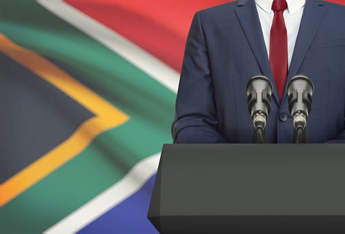 Businessman or politician making speech from behind the pulpit with national flag on background - South Africa