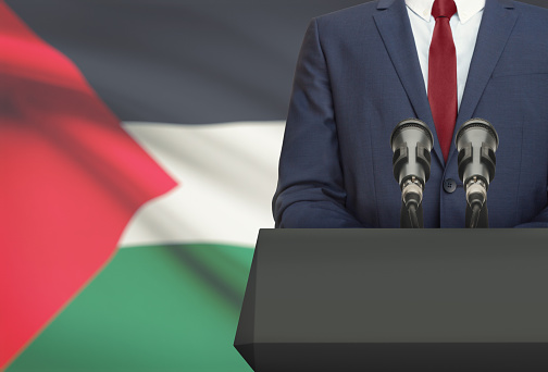 Businessman or politician making speech from behind the pulpit with national flag on background - Palestine