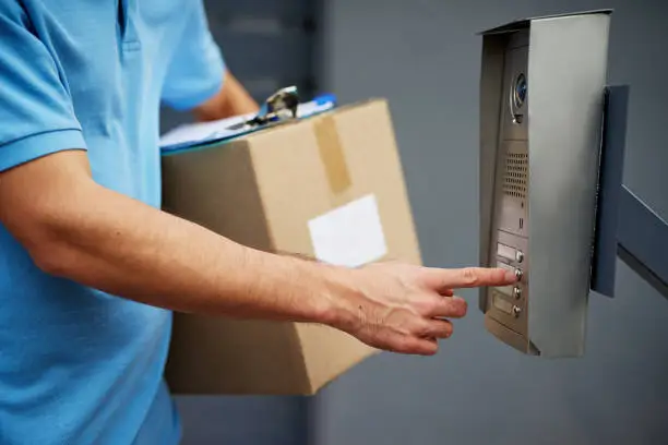 Closeup shot of a courier ringing an intercom while making a delivery