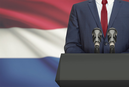 Businessman or politician making speech from behind the pulpit with national flag on background - Netherlands