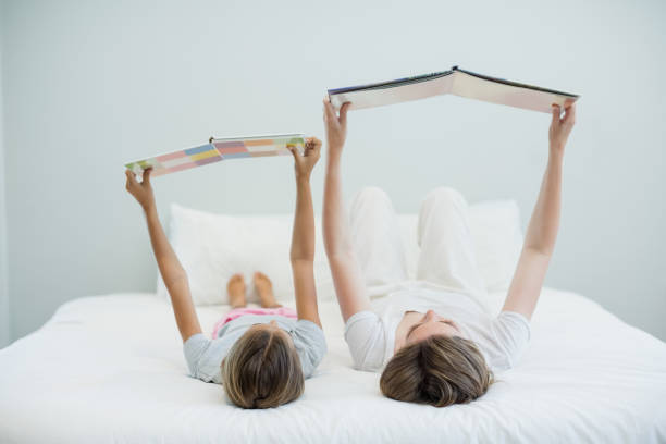 istock Mother and daughter lying on bed and reading book 667045284