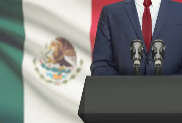 Photo of Businessman or politician making speech from behind a pulpit with national flag on background - Mexico