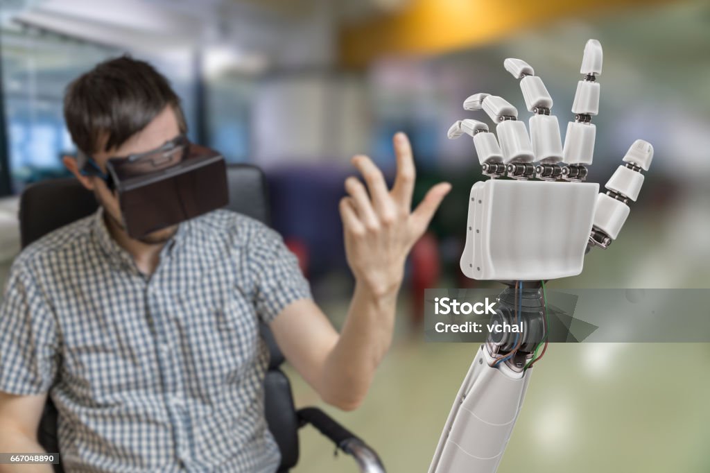 Young man is controlling robotic hand with virtual reality headset. Robotic Arm Stock Photo