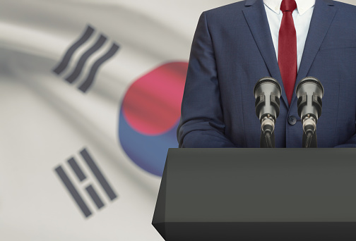 Businessman or politician making speech from behind the pulpit with national flag on background - South Korea